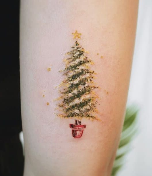 Menina com tatuagem em forma de pinheiro com uma estrela amarela;  Tatuagens para meninas que amam o Natal