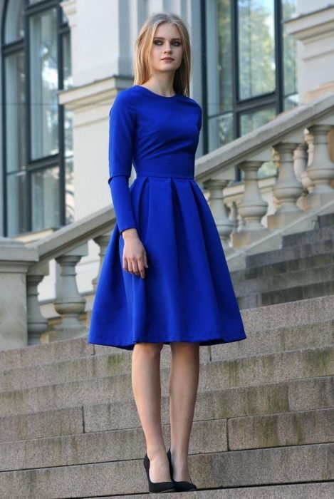Mulher loira na escada usando vestido curto azul royal de festa ou casual com mangas e salto preto