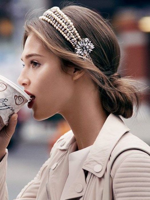Rapariga com casaco bege a beber café com o cabelo penteado adornado com diadema