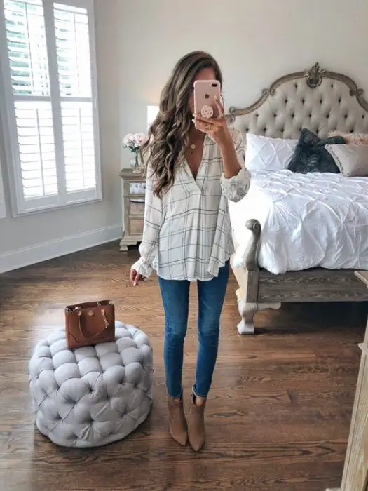 Garota de cabelos longos cacheados tira uma selfie em frente ao espelho com uma blusa xadrez justa e jeans