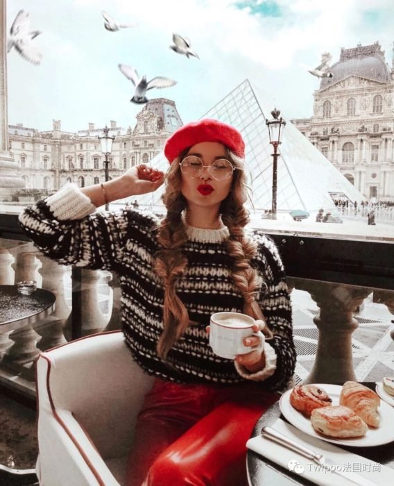 Rapariga sentada num café de Paris com uma camisola de Natal feia enquanto toma café 