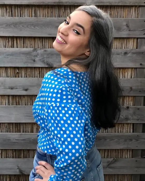 Garota de cabelos longos grisalhos posando para a fotografia e sorrindo, blusa azul com pontos brancos