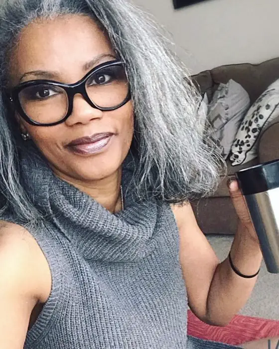 Morena, mulher afro-americana de óculos e tomando café em uma garrafa térmica, blusa de tricô cinza e cabelo curto grisalho