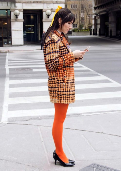 Trajes com meia-calça colorida;  garota de meias laranja e jaqueta xadrez, olhando para o celular na rua