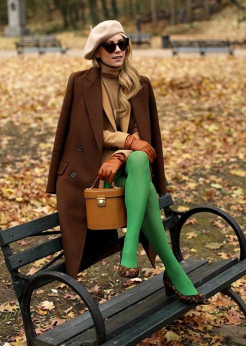 Trajes com meia-calça colorida;  mulher sentada no banco do parque, com boina francesa, óculos de sol, jaqueta marrom, meias verdes, sapatos com estampa animal