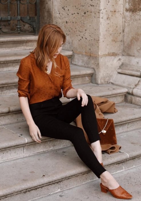 Traje formal e de escritório juvenil;  mulher ruiva sentada na escada com blusa laranja e calça tubo