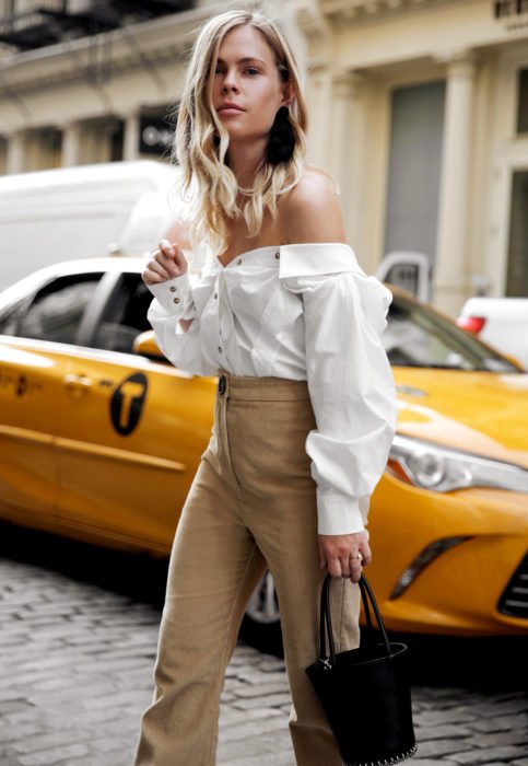Conjunto com blusa branca;  mulher loira na rua esperando táxi, vestindo camisa sem ombros