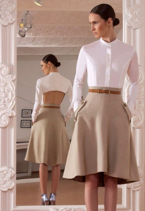 Conjunto com blusa branca;  mulher se olhando no espelho, com penteado elegante coque, camisa branca sem costas, saia bege