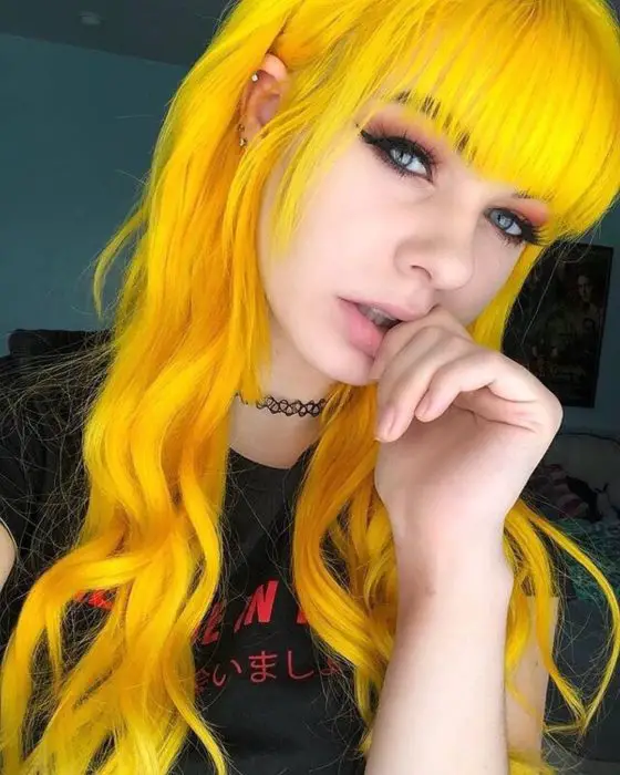 Menina com cabelo longo, ondulado, com franjas e amarelo brilhante