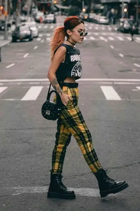 Menina andando pela rua com uma blusa preta e calças xadrez amarelas