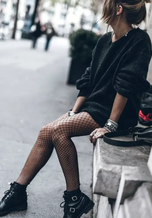 Menina sentada de vestido preto e meias arrastão