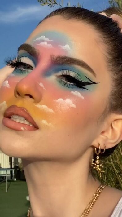 Maquiagem estética em tons de arco-íris e nuvens no rosto
