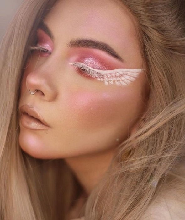 Maquiagem estética em tons de rosa e branco com asas de anjo nos olhos
