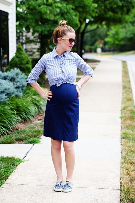 Menina grávida com saia azul e blusa branca com linhas 
