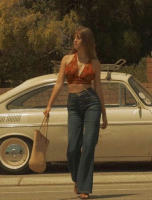 Moda feminina dos anos 70;  menina andando na rua com calça larga na cintura, top vermelho com flores amarelas;  roupa retro