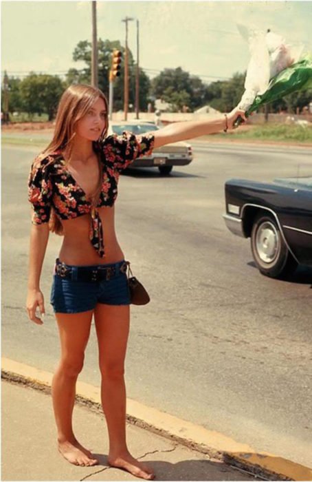 Moda feminina dos anos 70;  mulher pedindo rait com um buquê de flores, shorts curtos, preto floral, descalço;  penteado retro e roupas