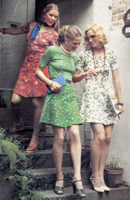 Moda feminina dos anos 70;  amigos descendo escadas, vestidos com flores acima do joelho, vermelhos, brancos e verdes, com sandálias;  penteados e roupas retrô