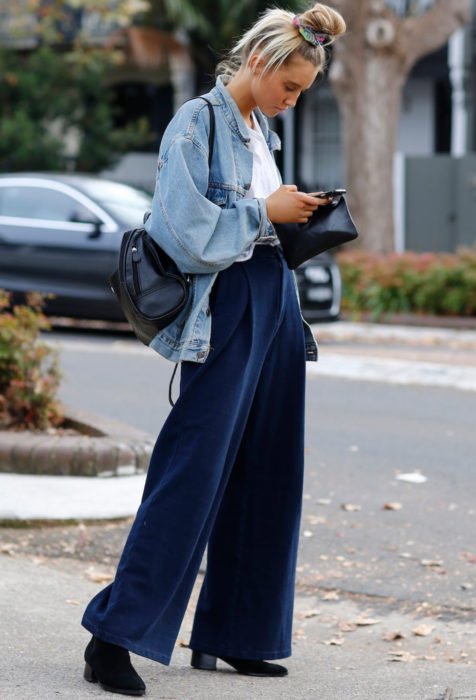Looks com jeans largos;  loira olhando para o celular na rua com calças largas e penteado com coque alto