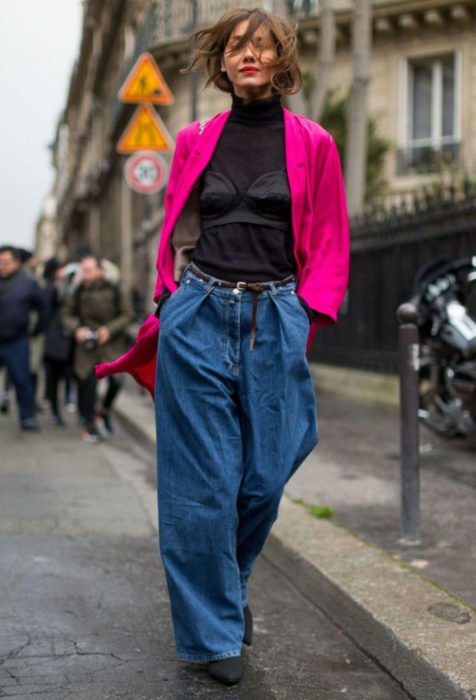Looks com jeans largos;  mulher com look maluco, jaqueta fuscia rosa, blusa de gola alta, calça grande demais, garota andando na rua com as mãos nas bolsas