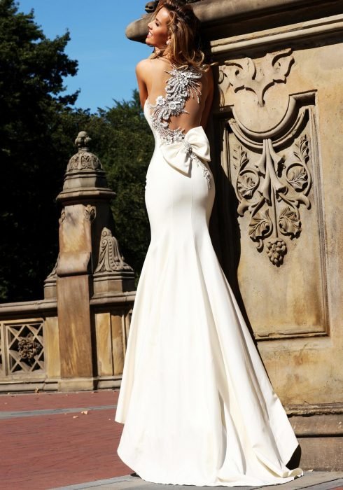 Menina com um vestido de noiva com decote nas costas em pé sobre uma coluna de pedreira 