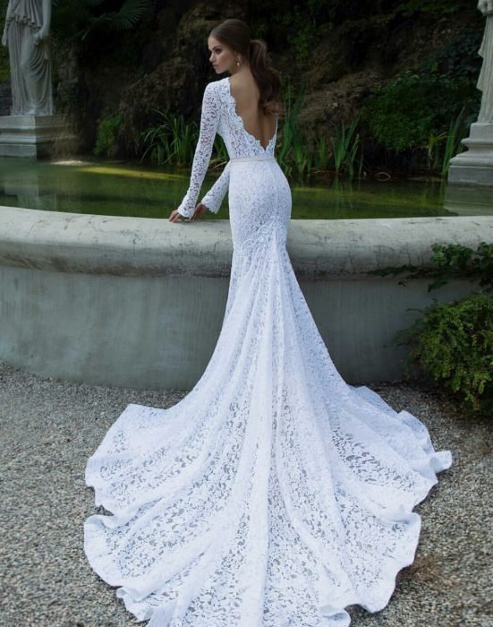 Menina com um vestido de noiva com decote nas costas em frente a uma fonte 
