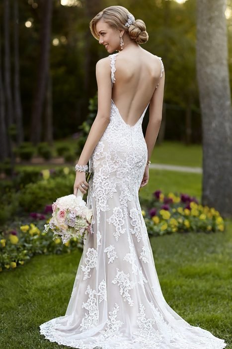Menina com um vestido de noiva com decote nas costas parada do lado de fora em um jardim 