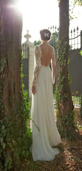 Menina em um vestido de noiva com decote nas costas entre duas árvores 