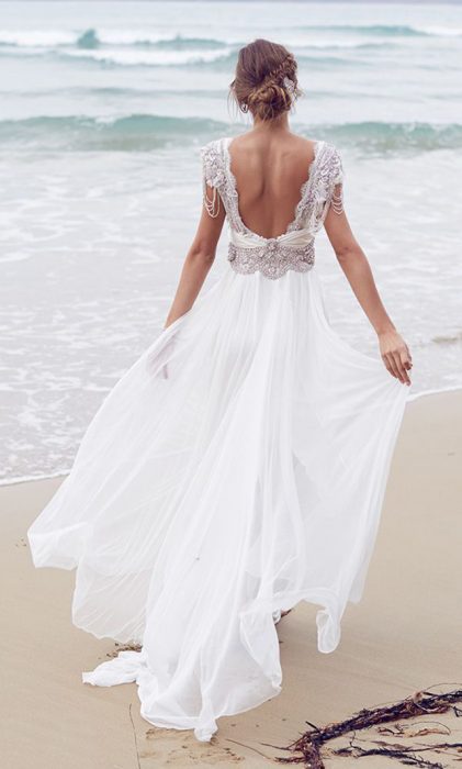 Menina com um vestido de noiva com decote nas costas caminhando na praia 