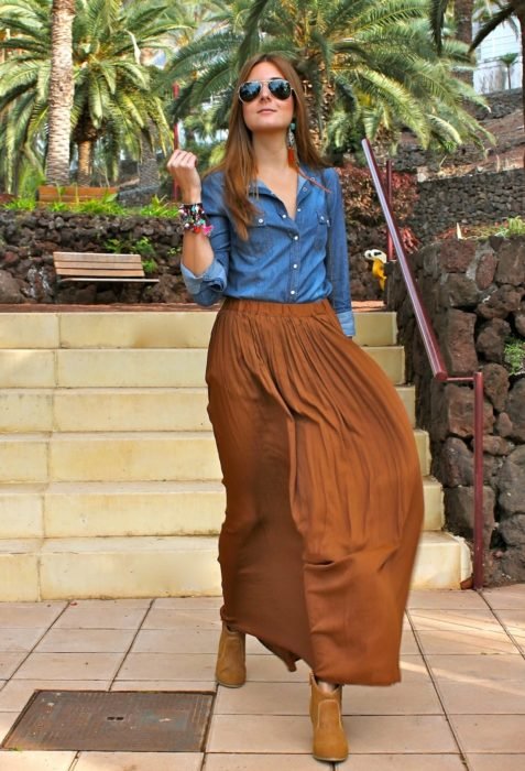 Menina vestindo uma saia marrom, blusa jeans azul e botins marrons 