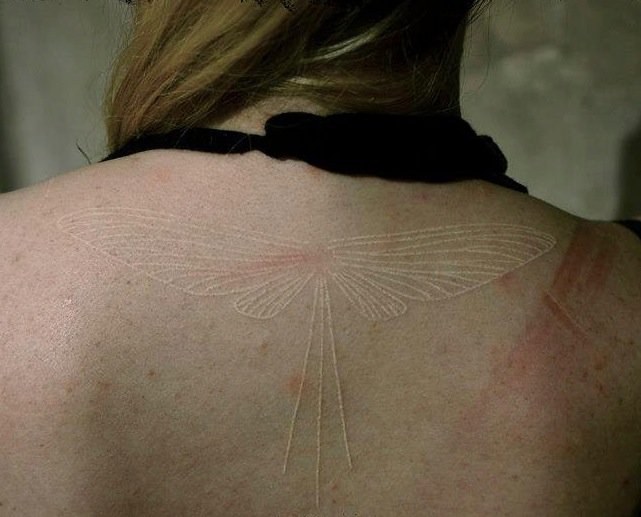 costas de uma garota com uma tatuagem de tinta branca que é uma libélula 