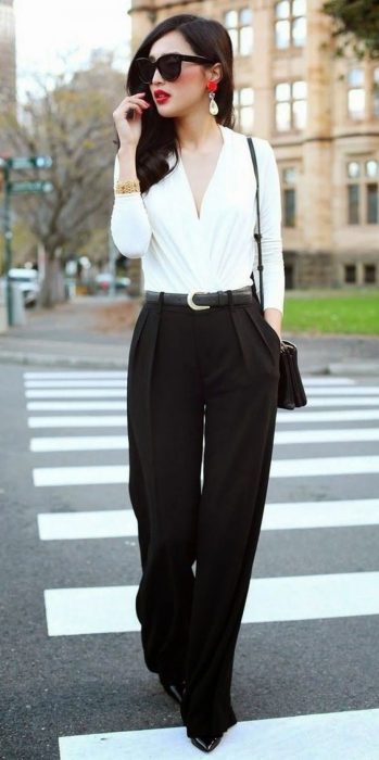 Garota de calça preta com blusa branca parada no meio da rua 