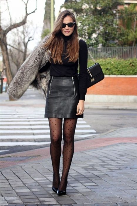 Garota na rua com uma saia de couro, suéter preto e sapatos de salto alto