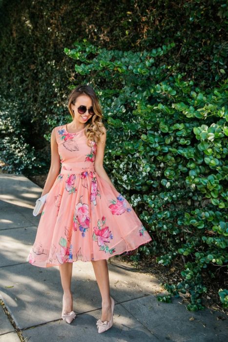 Idéias de vestidos para casamento em jardim ao ar livre;  garota ao lado de uma trepadeira em vestido de tule rosa com flores, sapatos de salto alto com laço e óculos de sol redondos