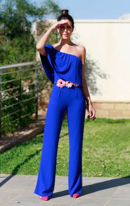 Idéias de vestido de casamento para jardim ao ar livre;  Mulher de cabelos castanhos com coque alto, cobrindo o sol com a mão, vestindo um macacão longo azul royal, com cinto de flores