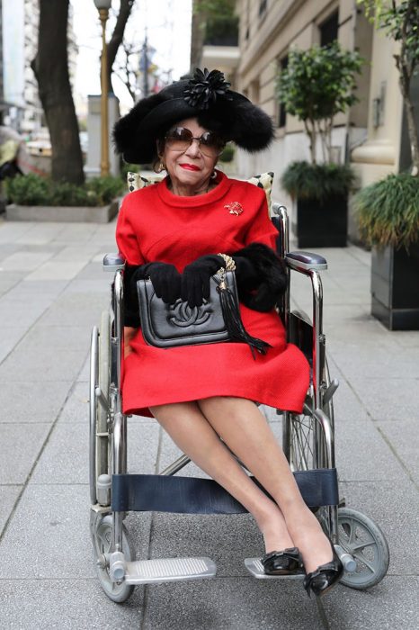 Mulher idosa em cadeira de rodas com vestido vermelho e bolsa chanel 