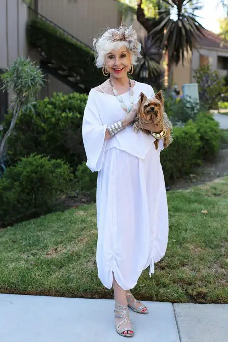 Mulher idosa vestindo um terno branco e segurando um cachorro 