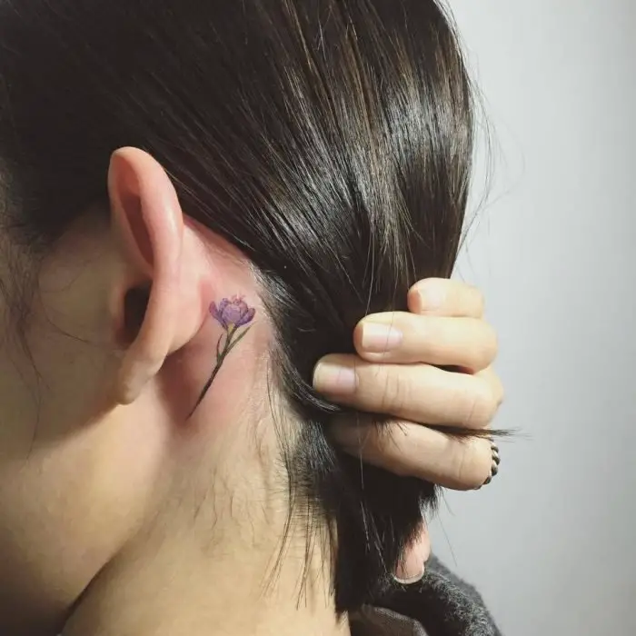 Menina com uma tatuagem atrás da orelha em forma de flor roxa