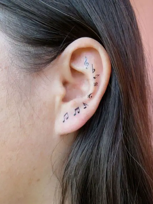Menina com uma tatuagem atrás da orelha em forma de letras musicais 