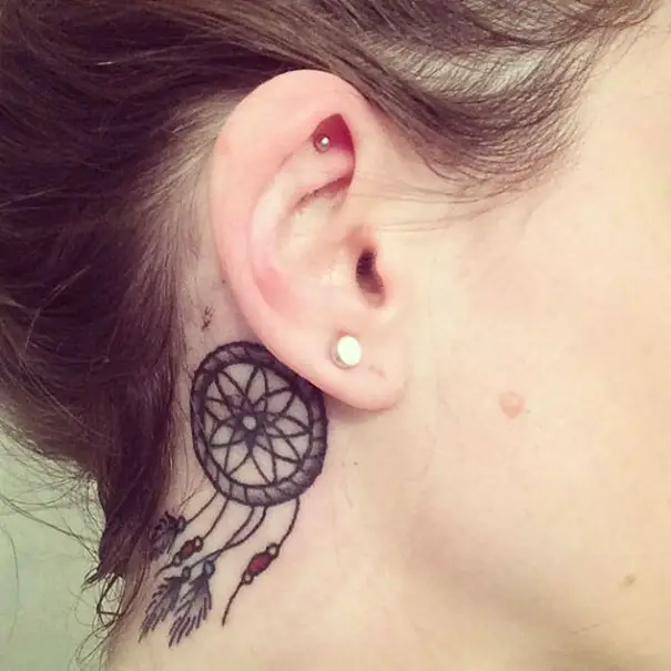 Menina com uma tatuagem atrás da orelha na forma de um apanhador de sonhos