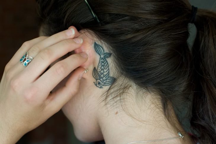 Menina com uma tatuagem atrás da orelha em forma de peixe-coi