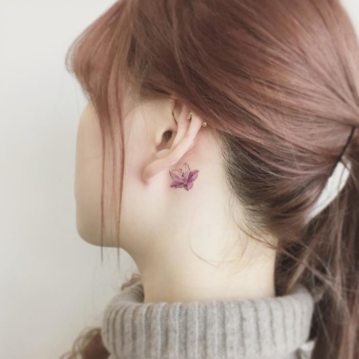 Menina com uma tatuagem atrás da orelha no formato de uma flor rosa