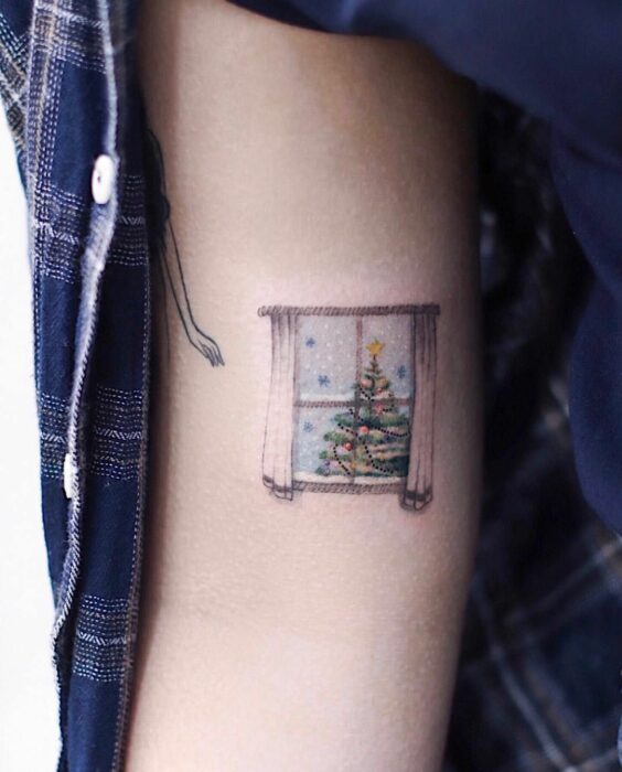 Menina com uma tatuagem de janela com uma árvore de Natal;  Tatuagens em miniatura para quem ama o Natal