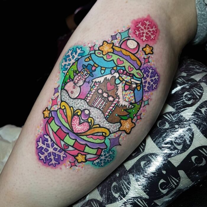 Menina com tatuagem de bola de cristal inspirada em uma cabana de Natal;  Tatuagens para meninas que amam o Natal