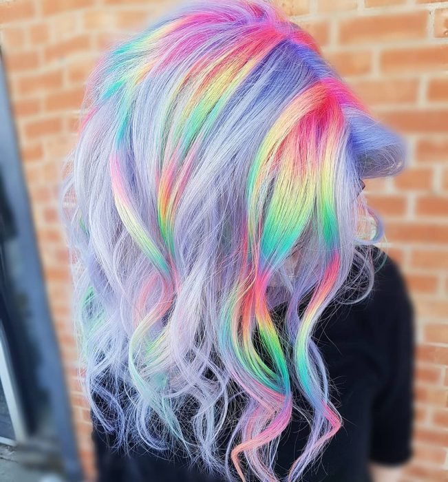 Menina com longos cabelos ondulados de cores lilás com reflexos amarelos, verdes, azuis e rosa