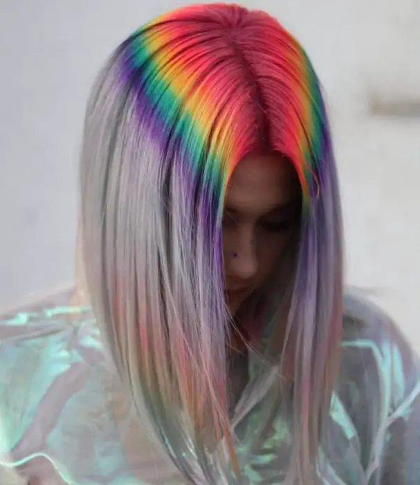 Menina de cabeça baixa e cabelos grisalhos com tintas fantasiosas na raiz simulando o reflexo de um arco-íris, vermelho, amarelo, verde e roxo