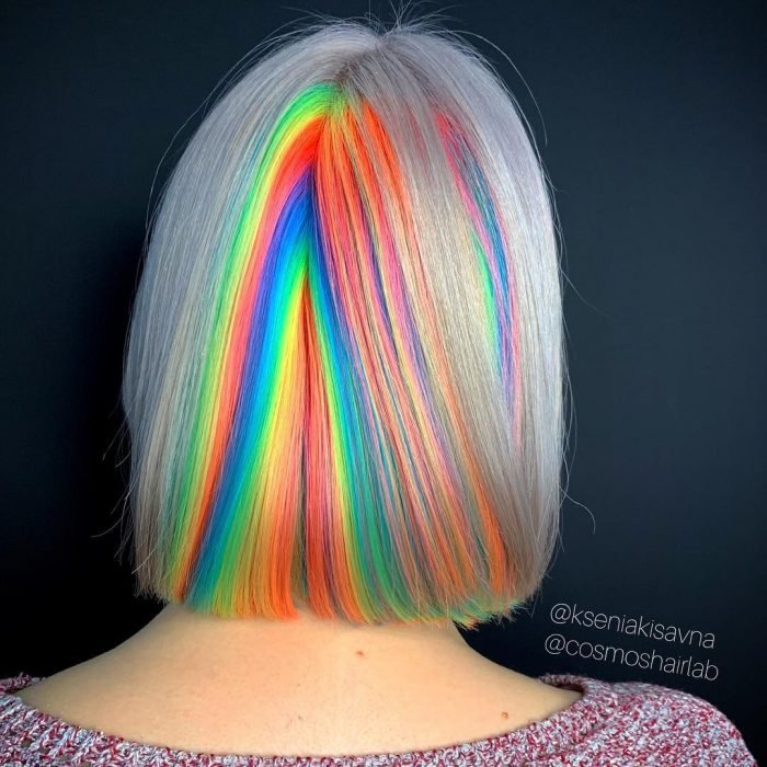 Rapariga de cabelo curto e liso, tingido em cores fantasia simulando o reflexo da luz, verde, laranja, azul e amarelo