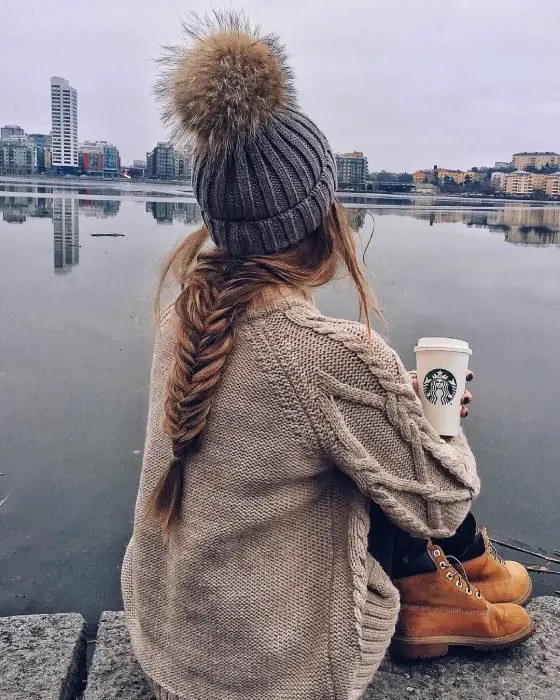Garota de cabelo comprido trançado com chapéu de inverno sentada e bebendo café