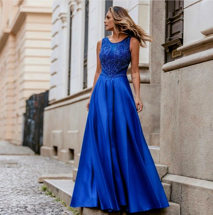 Mulher loira em pé nos degraus em um longo vestido de baile azul royal sem mangas com enfeites