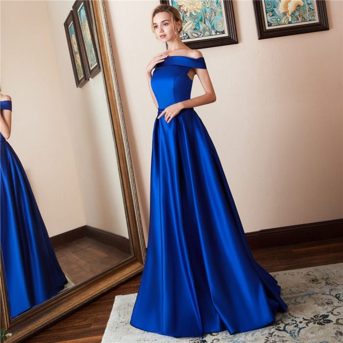 Rapariga loira em frente ao espelho com um vestido longo de cetim azul royal com ombros fora de casa