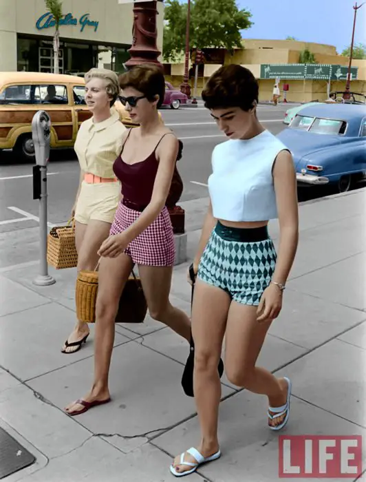 Moda feminina dos anos 70;  amigos andando na rua, shorts xadrez rosa e preto, diamantes azuis e verdes, roupas retrô;  corte de cabelo de duende